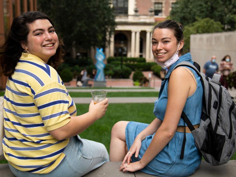 Students sit on campus with "Weecha" statue in the background